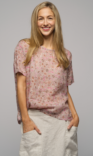 Close up of a woman wearing a short sleeved floral print blouse with a light cream coloured skirt, with big pockets.