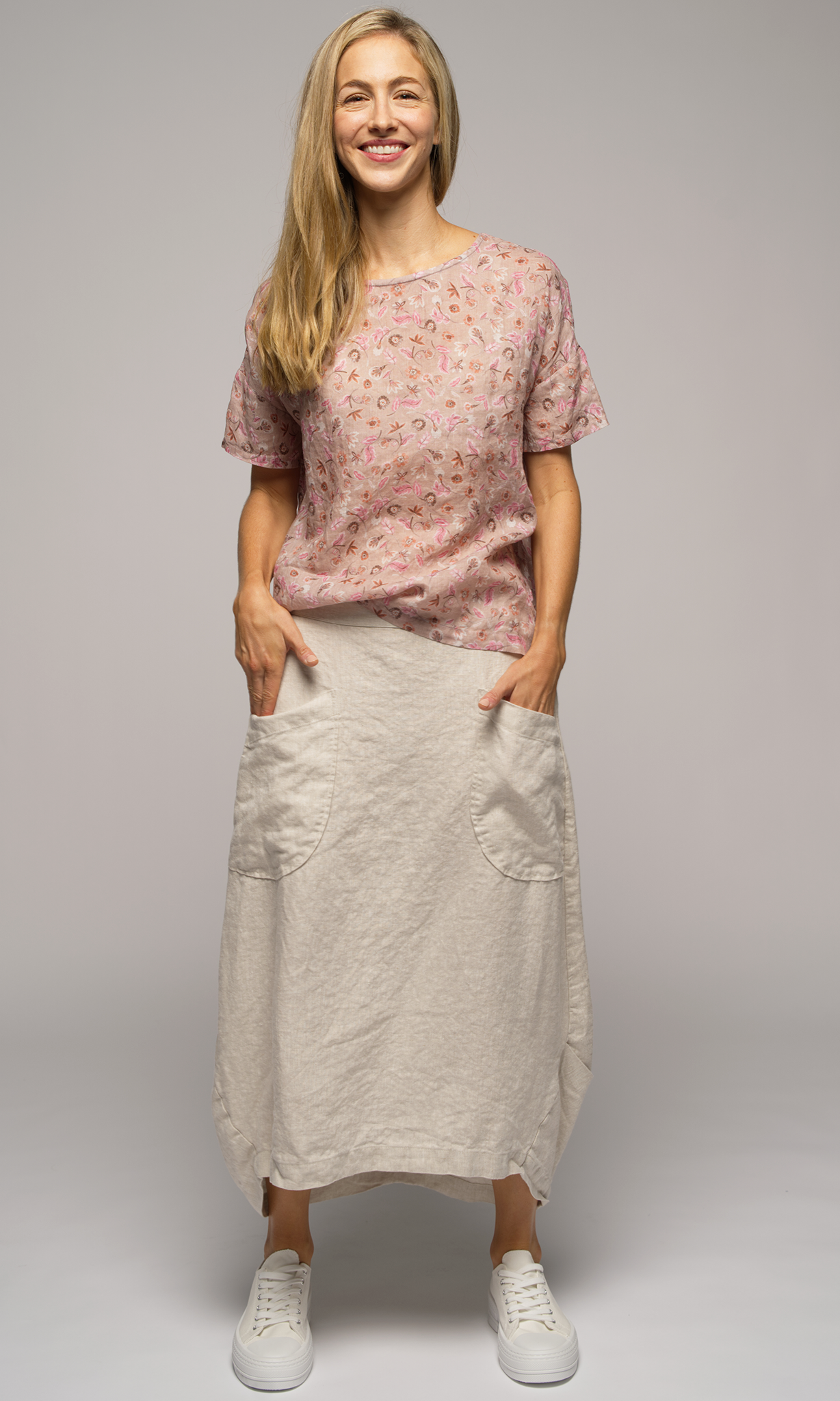 Woman wearing a short sleeved floral print blouse with a light cream coloured skirt, with big pockets.