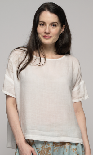 A close up of a woman wearing a white blouse with a blue patterned skirt.