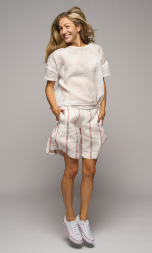 A women wearing a white short sleeve top with pink and white striped shorts, jumping in the air.