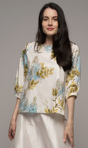 Woman wearing a floral blouse and white silk skirt.