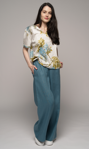 Woman wearing a floral blouse and teal pants.