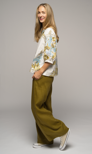 Woman wearing a floral blouse and wide-leg olive green pants, facing to the left.
