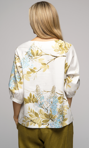 Woman wearing a floral blouse and wide-leg olive green pants, showing back of top.